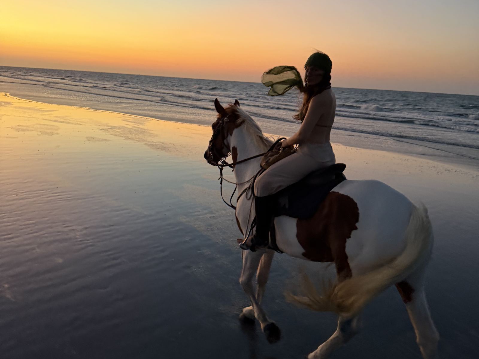 Lidiane Grigoletto a cavalo na beira-mar da Praia do Preá, com o céu laranja do pôr do sol refletido na areia molhada