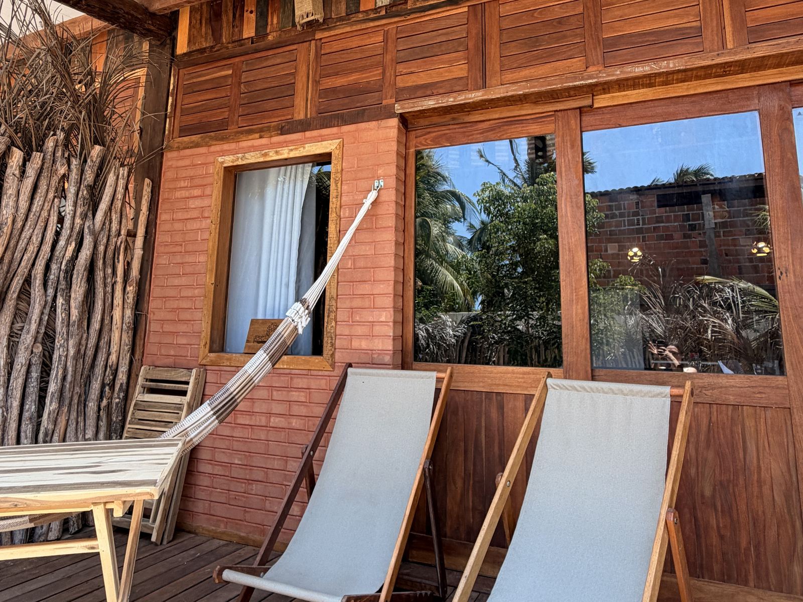 Varanda de madeira do Ecoloft da Vila Imbuía, no Preá, com rede e duas cadeiras de praia