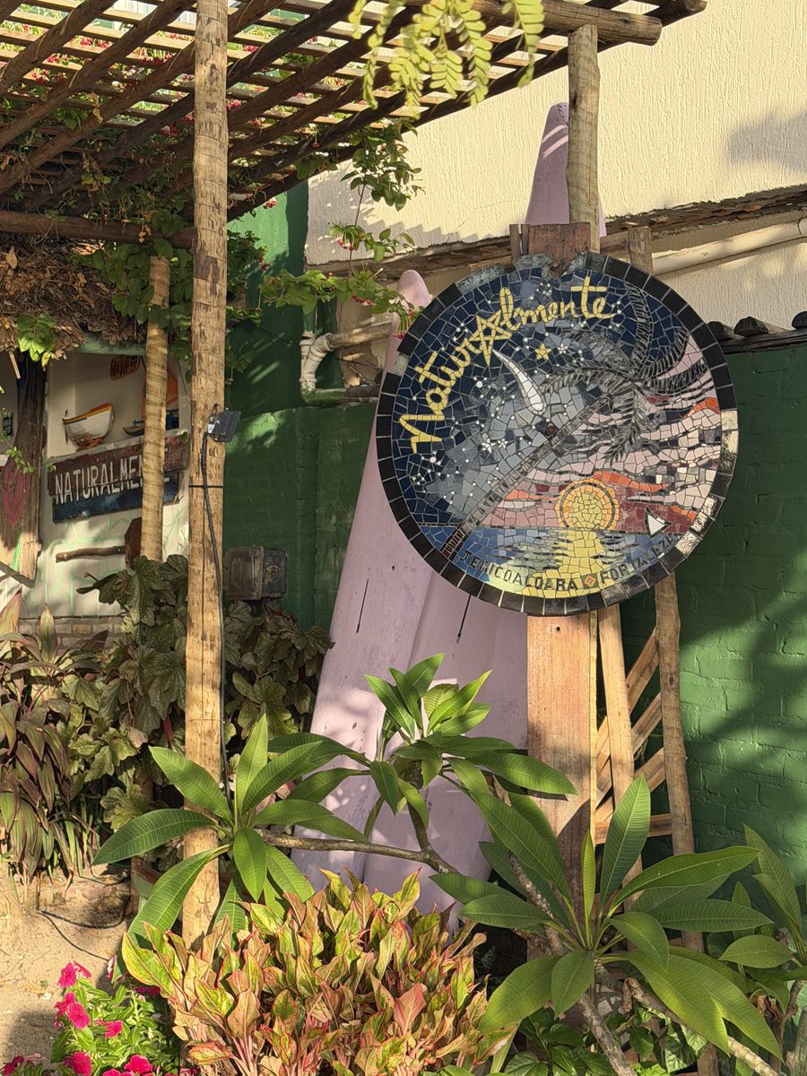 Placa do Café Naturalmente entre plantas, na entrada da rua principal de Jericoacoara