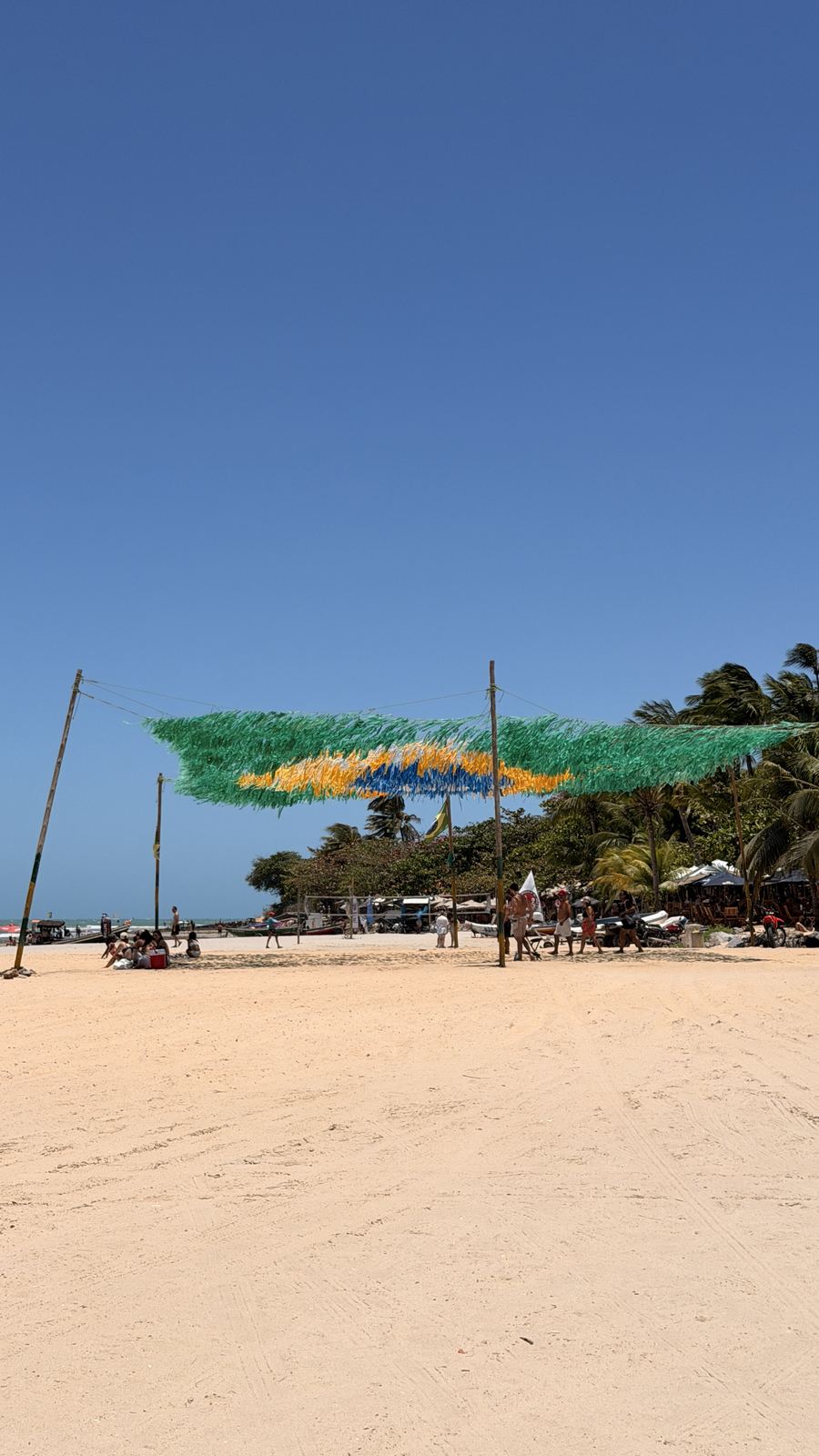 Bandeira do Brasil feita de fitas presa entre postes sobre a areia da Praia de Jericoacoara